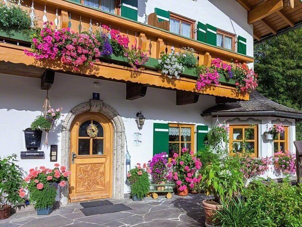 Una cabaña tradicional con puerta de madera, contraventanas verdes y macetas con flores en el balcón.