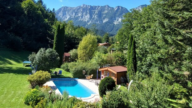 Un jardin avec une piscine, entouré d’une végétation luxuriante et offrant une vue sur les montagnes.