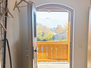 An open door leading to a balcony with a view of trees and a building.