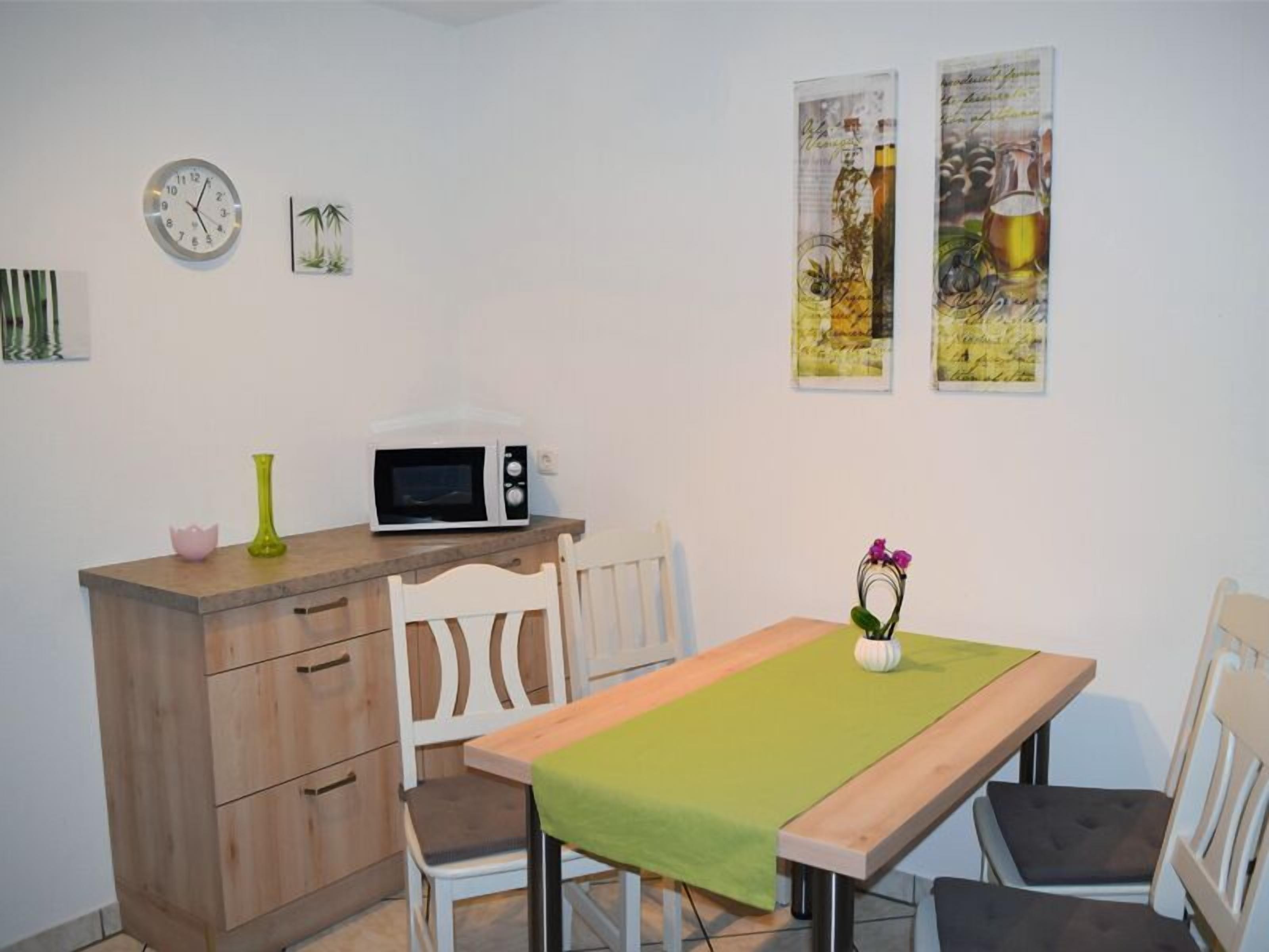 Ein kleiner Essbereich mit einem Holztisch, zwei Stühlen, einer Mikrowelle auf einer Holzplatte und Wandbildern.