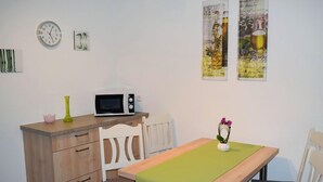 A small dining area with a wooden table, two chairs, a microwave on a wooden counter, and wall art.