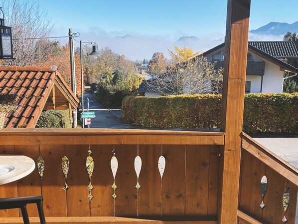 Una terraza de madera con barandilla y una mesa, con vistas a una calle residencial con casas y árboles.