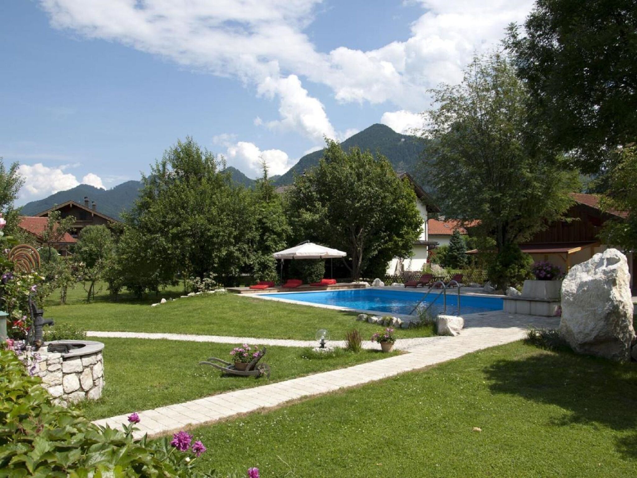 A backyard with a swimming pool, a covered seating area, and a stone well.