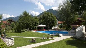 A backyard with a swimming pool, a covered seating area, and a stone well.