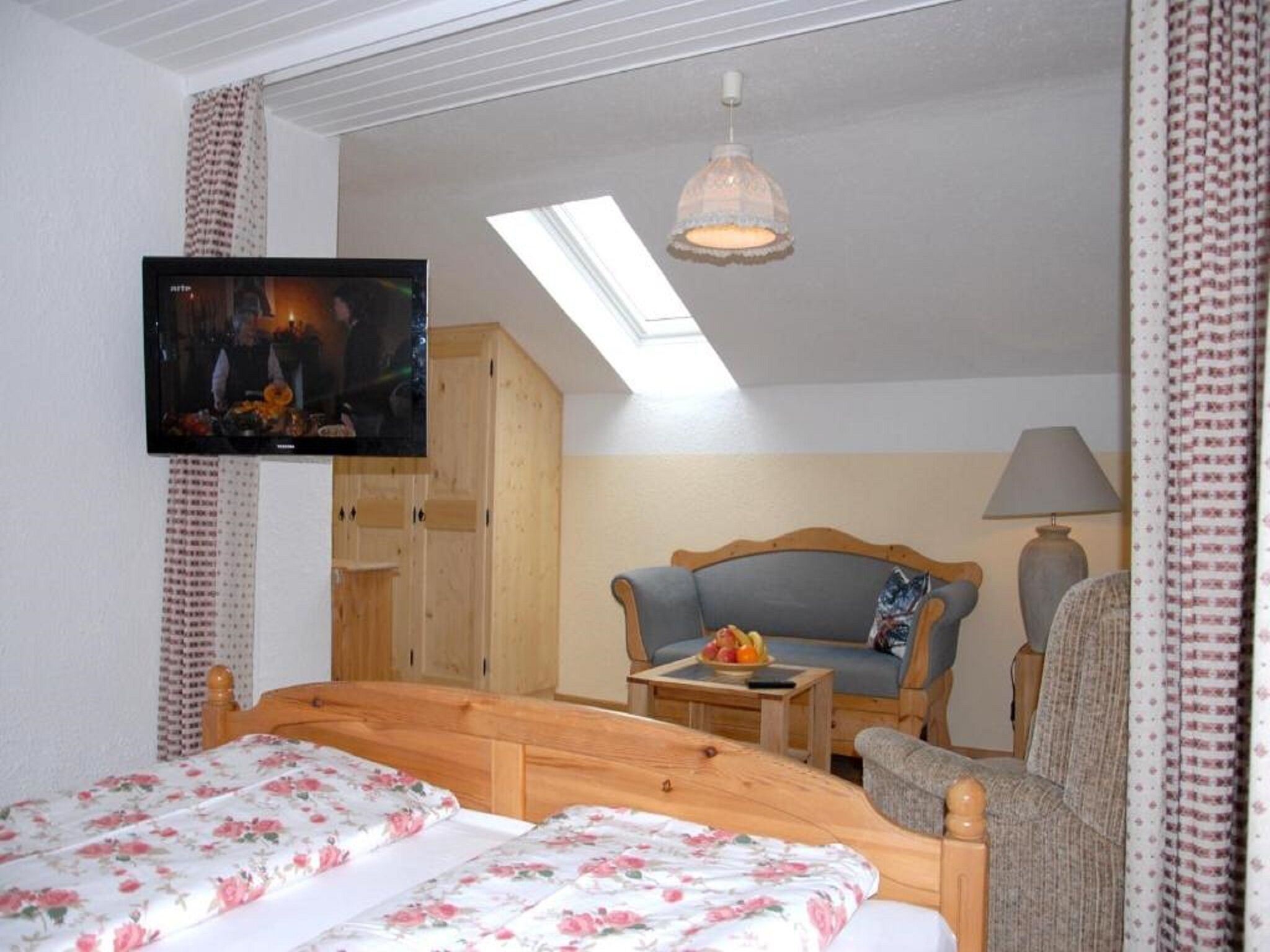 A bedroom with a bed, a sofa, a television, and a skylight.