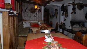 A rustic dining area with a wooden table, benches, and a fireplace. - 5. Fewo Kampenwand, 28 qm, 1-2 Pers., Wohn-Schlafraum, Westbalkon 2. OG (Grassau)