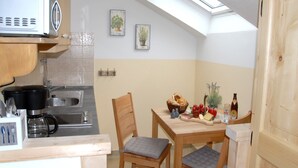 A compact kitchen with a microwave, sink, and wooden cabinets. A dining table with chairs is set under a skylight. - 5. Fewo Kampenwand, 28 qm, 1-2 Pers., Wohn-Schlafraum, Westbalkon 2. OG (Grassau)