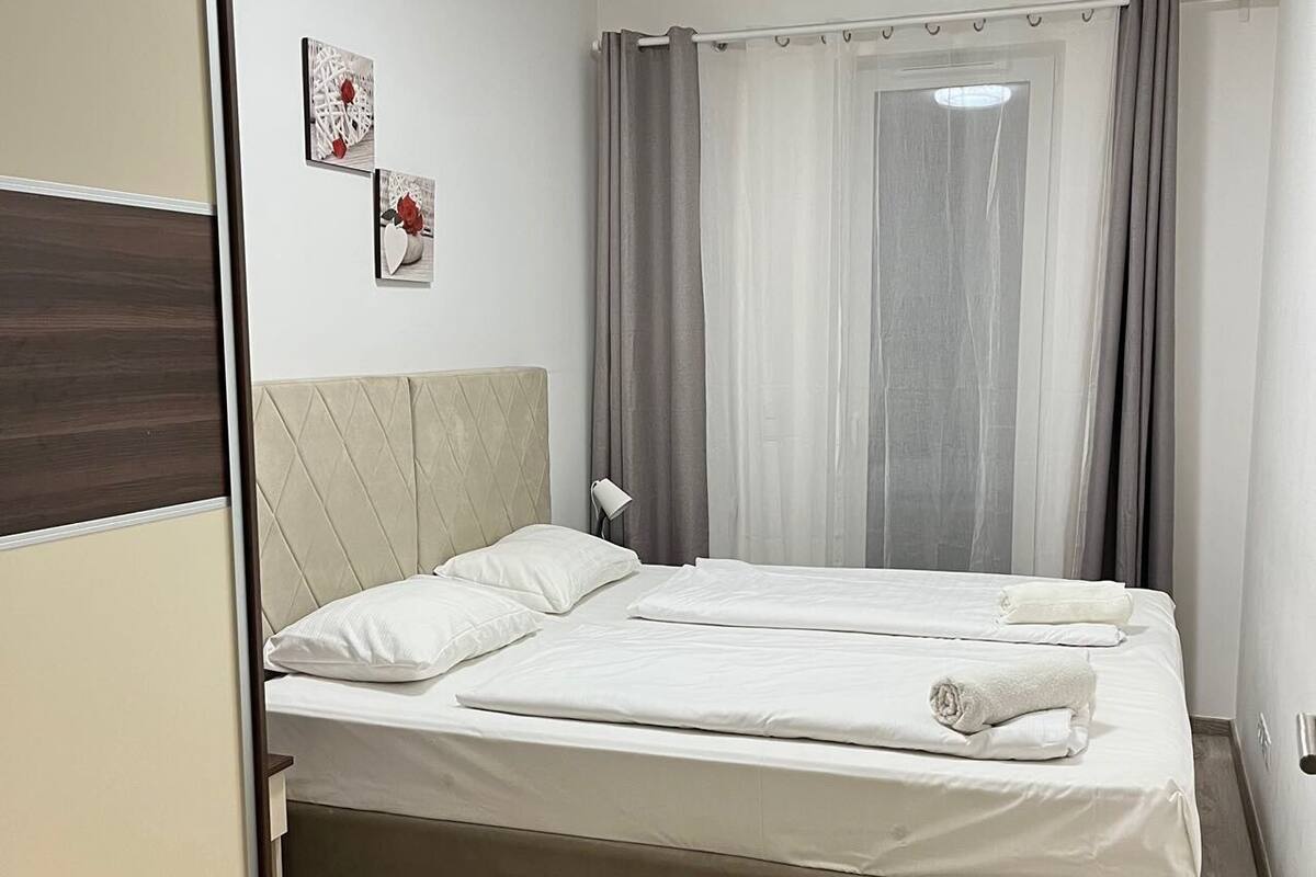 Un dormitorio con cama, mesita de noche, lámpara y ventana con cortinas.