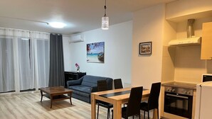 A modern living room with a sofa, dining table, and chairs. There is a kitchen area with an oven and a refrigerator. - Corvin Rose Apartment Hotel (Budapest)