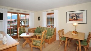 Ein gemütliches Zimmer mit einer Couch, Sesseln, einem kleinen Tisch und einem Fernseher.