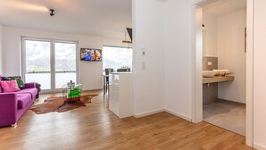 Una sala moderna con piso de madera, un sofá morado y un ventanal grande.