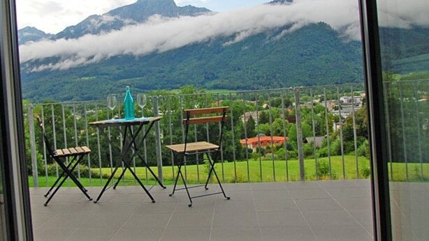 Un balcón con mesa y sillas, con vistas a un paisaje montañoso y nublado.