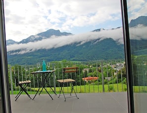 A balcony with a table and chairs, overlooking a mountainous landscape with clouds. - Apartment 2 Deluxe Studio, 52 sqm, 1-4 persons, 1 bedroom, living room and balcony (Bayerisch Gmain)
