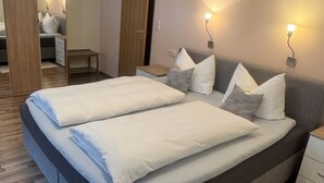 A double bed with white linens, a bedside table, a nightstand, and a mirror.