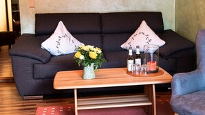 A living room with a dark sofa, two decorative pillows, a small wooden table with a vase of flowers, and a blue armchair.