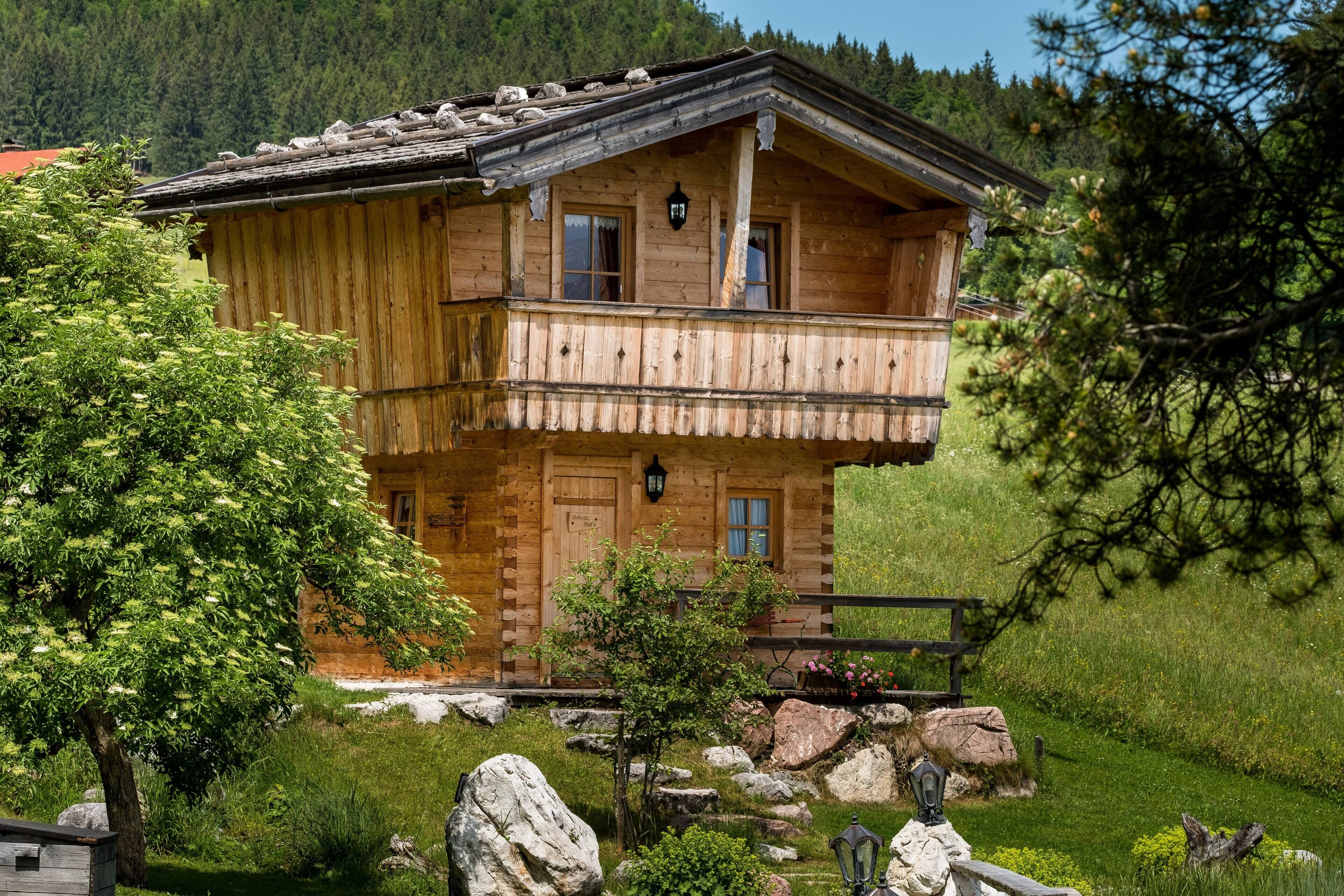 A two-story wooden cabin with a balcony, surrounded by a natural landscape.