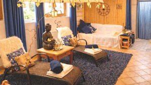 Een gezellige kamer met een houten plafond, een Boeddhabeeld, een witte bank en een blauw vloerkleed.