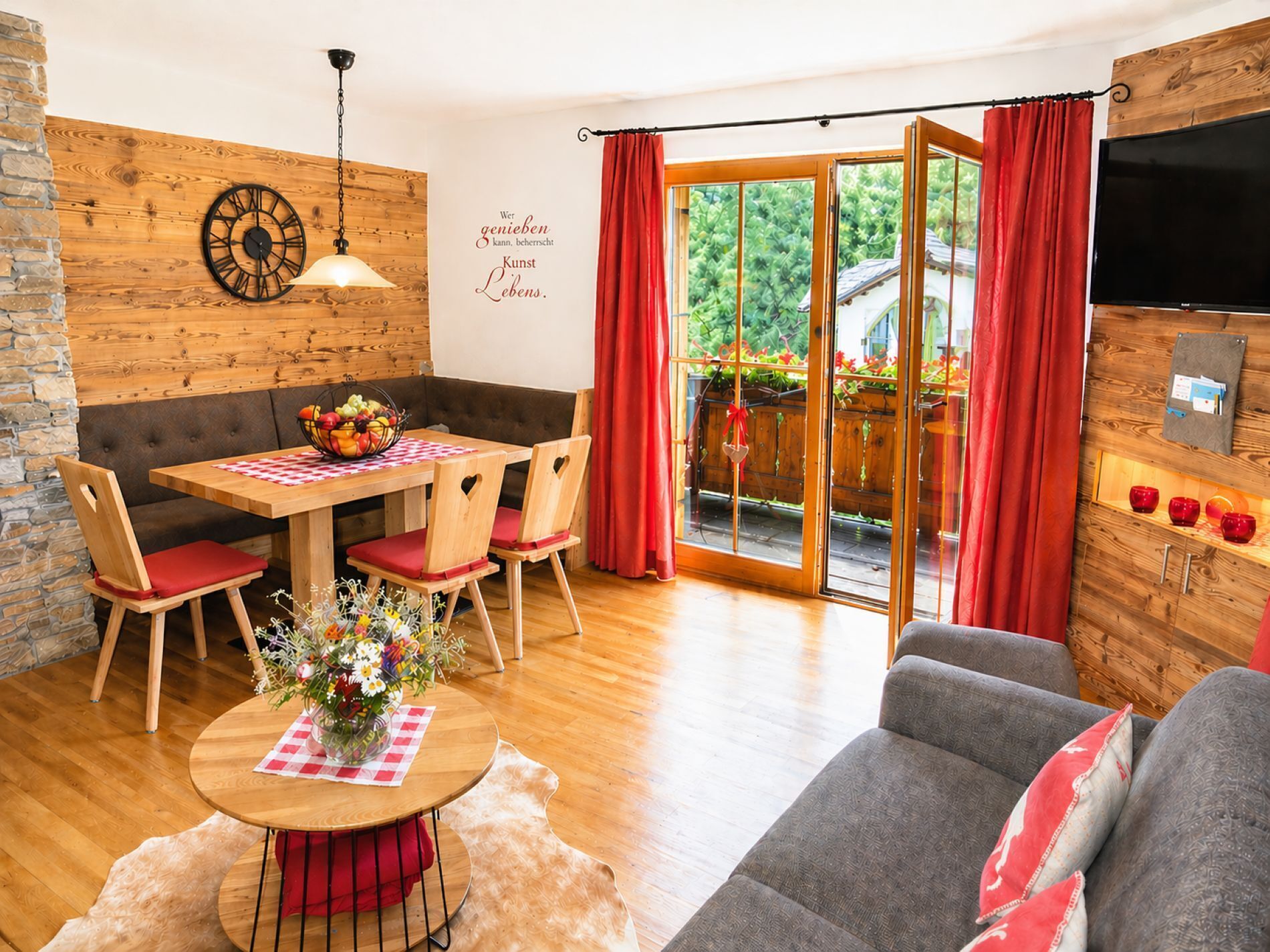A cozy room with a wooden wall, a dining table with chairs, a sofa, and a TV mounted on the wall.