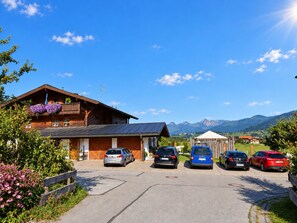 Un bâtiment en bois doté d’un balcon, avec des voitures garées devant et une vue sur la montagne.