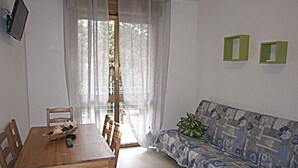 Una habitació amb taula de dinar de fusta, cadires, un sofà i televisió penjada a la paret.