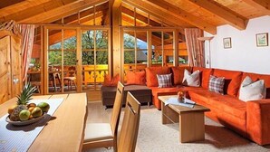 A cozy cabin interior with a wooden ceiling, a dining area with a table and chairs, a sofa set, and large windows offering a view of the outdoors. - Ferienwohnung Watzmann für 2-7 Personen, ca. 90 m², 2 sep. Schlafzimmer, Wohnküche, Balkon, 2 Zustellbetten (Bischofswiesen)
