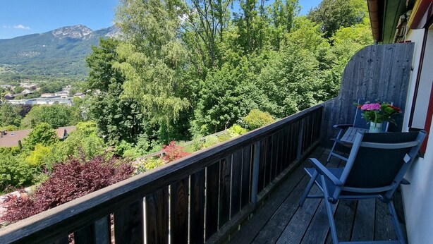 Een balkon met een houten hekwerk, een tafel met stoelen en een bloevas.