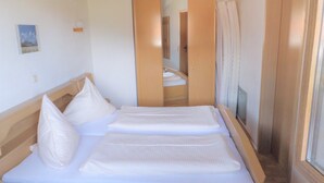 A bedroom with a wooden bed frame, two pillows, a bedside table, and a mirror. - Vacation apartment C, 4 pers. with balcony or terrace, bedroom, 40 to 45 sqm (Inzell)