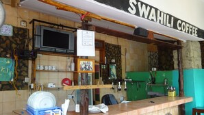 A coffee shop interior with a counter, shelves, a television, and a sign that reads "SWAHILI COFFEE". - Homeland Swahili Lodge - Hostel (Nungwi)