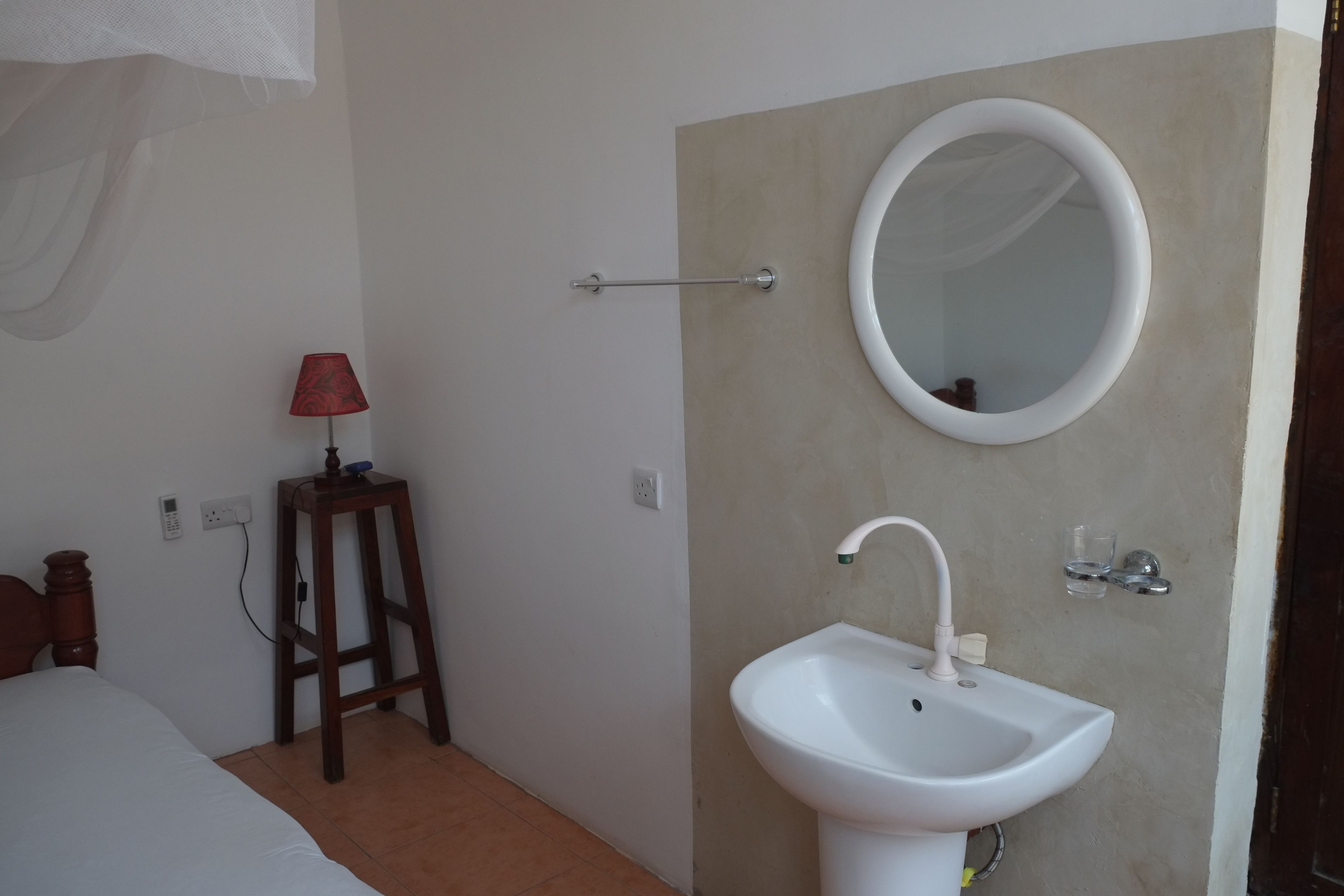 A bathroom with a white sink, a mirror, a red lamp, and a wooden stool.