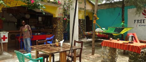 An outdoor dining area with a wooden table and chairs, a hammock, and a small table with a red tablecloth.