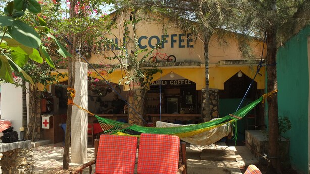 A hammock chair with red checkered cushions in a shaded outdoor area with a building labeled "SAHLI COFFEE" in the background. - Homeland Swahili Lodge - Hostel (Nungwi)