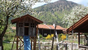 Une aire de jeux avec un toboggan et des structures d’escalade, entourée d’une clôture en bois et d’arbres.