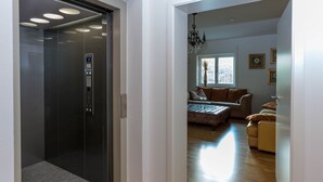A modern elevator with a digital display and a glass door, leading to a living room with a sofa, a coffee table, and a chandelier. - Deluxe loft 150 sqm with 2 bedrooms for 1-6 persons and balcony (Bad Reichenhall)