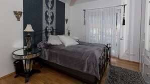 A bedroom with a bed, a round glass table, a wall with a large abstract painting, and a door with a curtain. - Deluxe loft 150 sqm with 2 bedrooms for 1-6 persons and balcony (Bad Reichenhall)