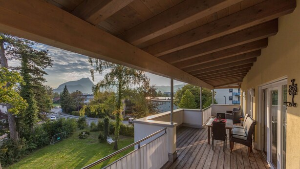 A wooden deck with a table and chairs, overlooking a green landscape and a mountain in the distance. - Deluxe loft 150 sqm with 2 bedrooms for 1-6 persons and balcony (Bad Reichenhall)