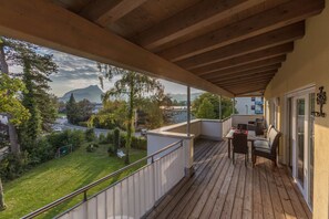 Une terrasse en bois avec une table et des chaises, d’où l’on peut admirer un paysage verdoyant et une montagne au loin.
