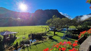 Una vista panorámica de un campo verde con una estructura de madera, un pequeño estanque y una montaña al fondo.