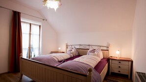 Ein Schlafzimmer mit schrägen Wänden, einem hölzernen Bett mit Kopfteil, zwei Nachttischen mit Lampen und einem Fenster mit Vorhängen.
