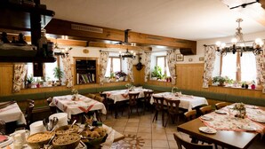 Ein gemütliches Restaurant mit Holzwänden und grün gepolsterten Bänken. Die Tische sind mit weißen Tischdecken und Kerzen gedeckt.
