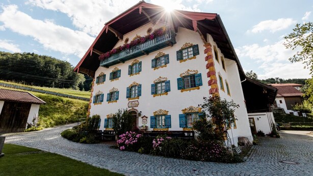 Ein traditionelles Gebäude mit einem geneigten Dach, mehreren Fenstern mit Fensterläden und einem Balkon mit Blumen.