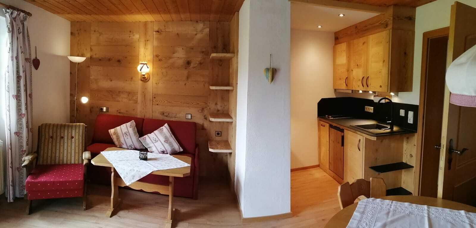 Una habitación acogedora con techo de madera, un sofá rojo, una mesita y una zona de cocina con armarios de madera y un lavabo.