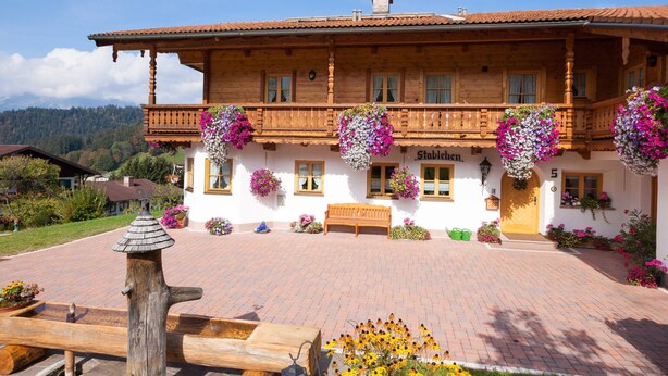 Un bâtiment traditionnel en bois, doté d’un balcon, de jardinières et d’un banc.