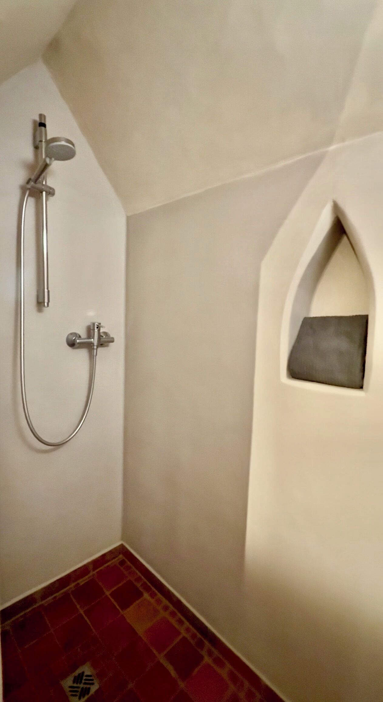 A bathroom with a shower, a towel rack, and a small alcove with a towel.