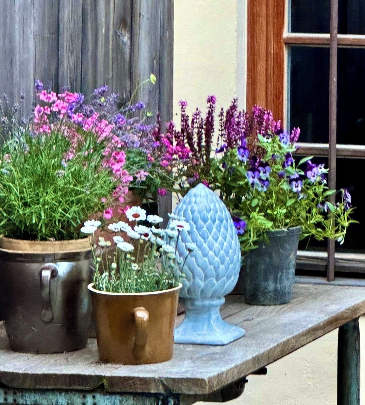 Una mesa de madera con varias macetas y un jarrón azul decorativo.