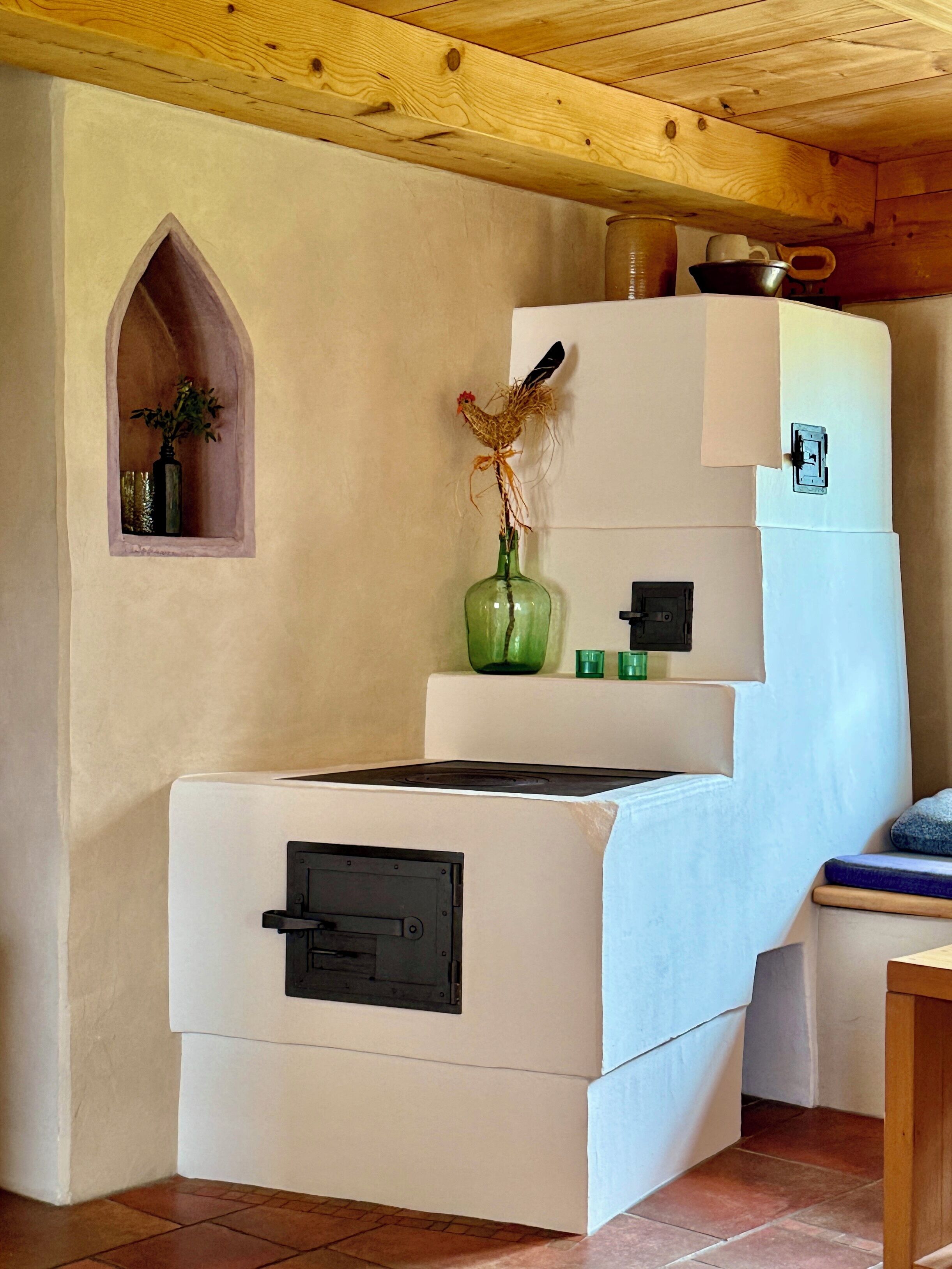A kitchen with a built-in stove, a small alcove with a plant, and a rustic wooden ceiling.