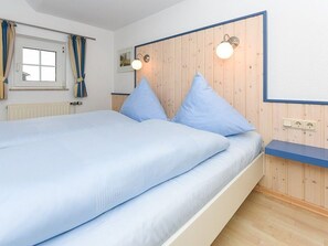 Une chambre à coucher avec un lit, une tête de lit en bois, des lampes de chevet, une fenêtre avec des rideaux et un radiateur.