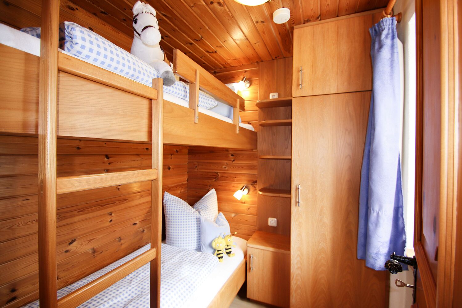 Uma cabana de madeira com beliches, um pequeno armário e uma cortina pendurada.