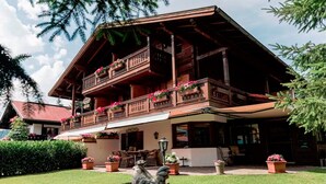 A wooden chalet with a balcony adorned with flowers, a lawn, and outdoor furniture. - (8) Vier-Raum-Ferienwohnung 85qm, 2 Bäder, 3 Schlafzimmer, Küche und Balkon (Reit im Winkl)