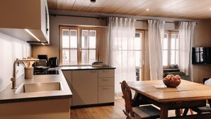 A modern kitchen with wooden cabinets, a stainless steel sink, and a dining area with a wooden table and chairs. - (8) Vier-Raum-Ferienwohnung 85qm, 2 Bäder, 3 Schlafzimmer, Küche und Balkon (Reit im Winkl)