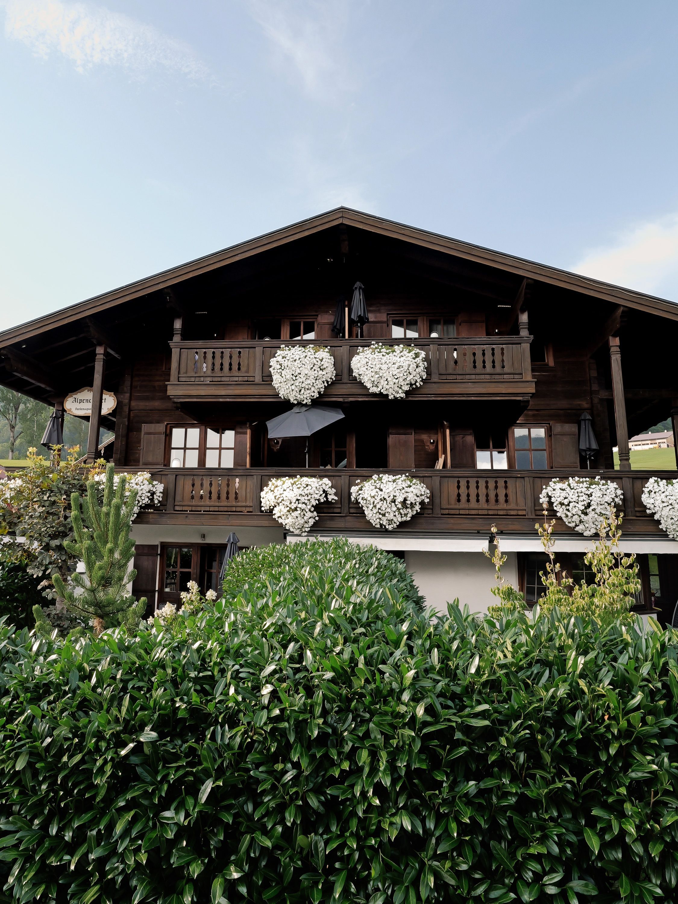 Un chalet en bois doté d’un balcon, de grandes fenêtres et de compositions florales en forme de cœur.